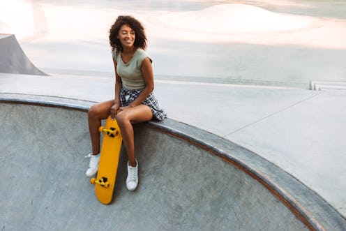 Smiling young afro american girl sitting with skateboard at a park