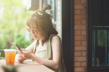 Portrait of cute asian teen woman using smartphone at coffee cafe. texting with someone. reading ple...