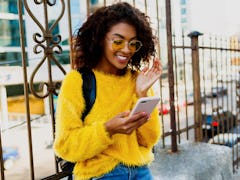 Outdoor image of young attractive American student woman with stylish hairs using mobile phone and s...