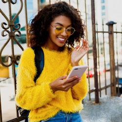 Outdoor image of young attractive American student woman with stylish hairs using mobile phone and s...