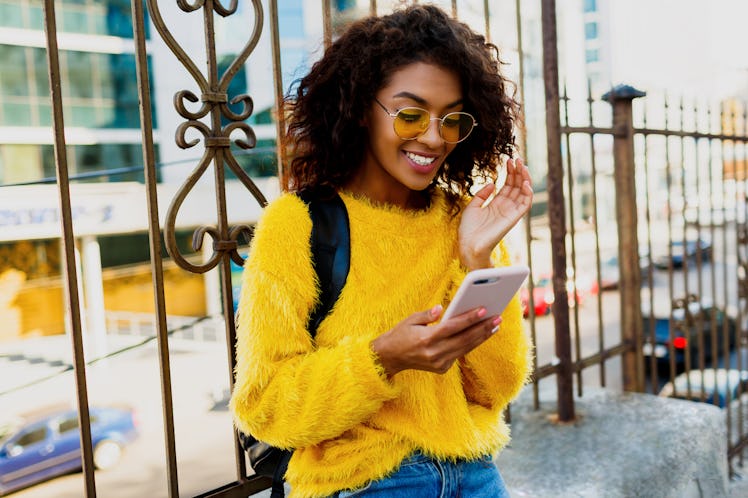 Outdoor image of young attractive American student woman with stylish hairs using mobile phone and s...
