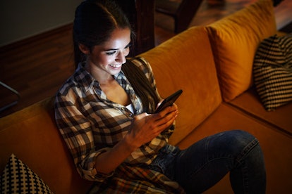 Attractive woman sitting at home on pleasant evening and chatting with friends on smart phone.