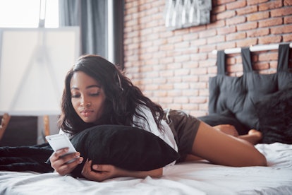 Portrait of beautiful woman waking up in her bed and looks into the phone. Check social networks, se...