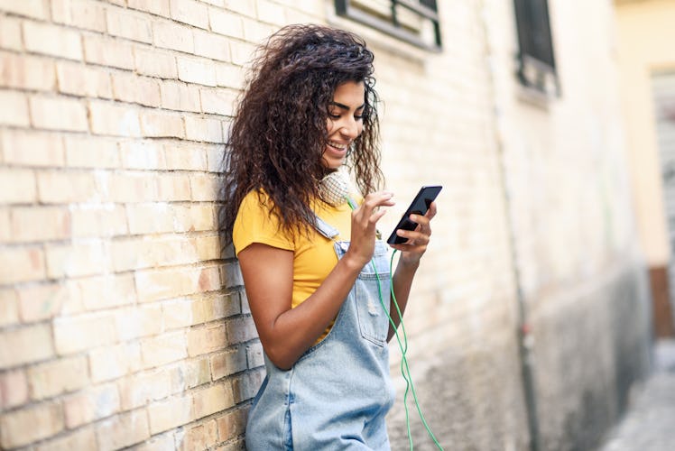 Young North African woman texting with her smart phone outdoors. Smiling Arab girl in casual clothes...