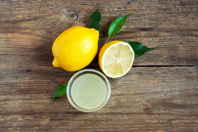 Fresh lemon juice in small bowl and lemons over rustic wooden background with copy space - healthy ingredient for cooking and baking