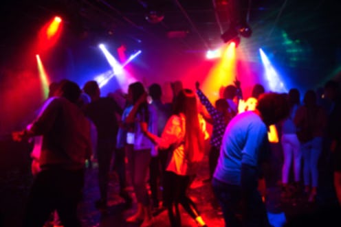 blurred silhouettes of a group of people dancing in a nightclub on the dance floor under colorful sp...