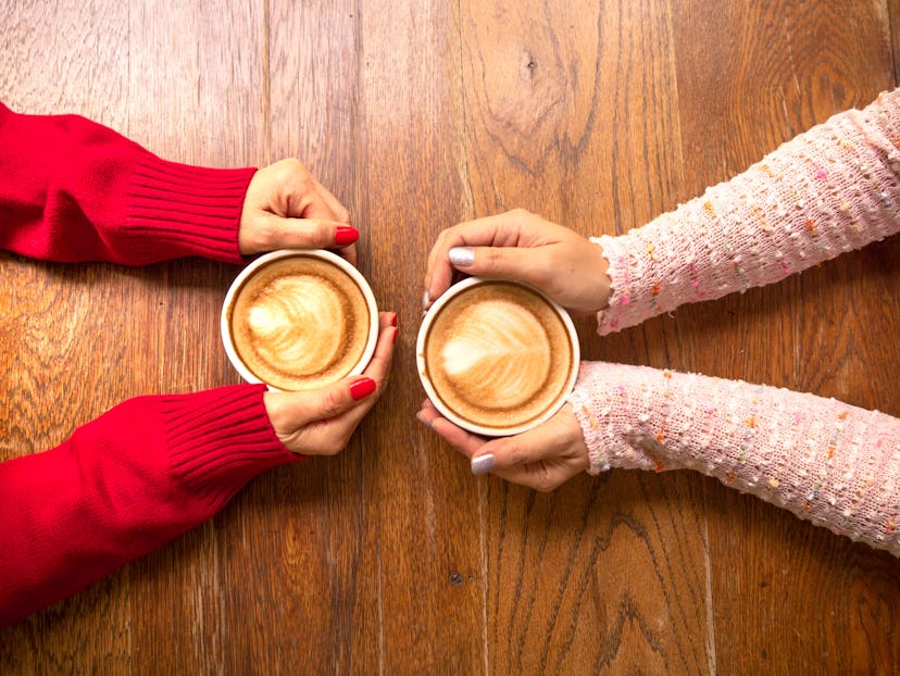 Two female hands holding cup of coffee a wooden vintage table in a coffeeshop, friend drink coffee