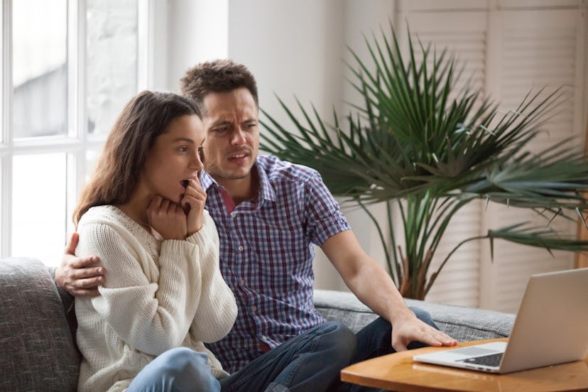 Scared man embracing shocked woman watching thrilling horror film or scary movie on laptop together,...