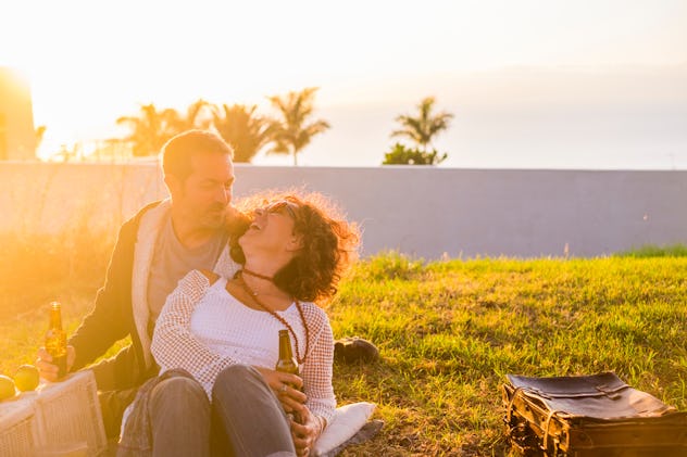 Couple laughing in love during picnic on the meadow for outdoor leisure activity together - married ...