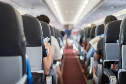 passenger seat, Interior of airplane with passengers sitting on seats and stewardess walking the ais...