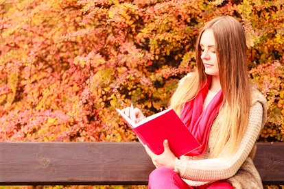 Woman fashion girl relaxing in autumnal park reading book sitting on bench. Fall lifestyle concept.