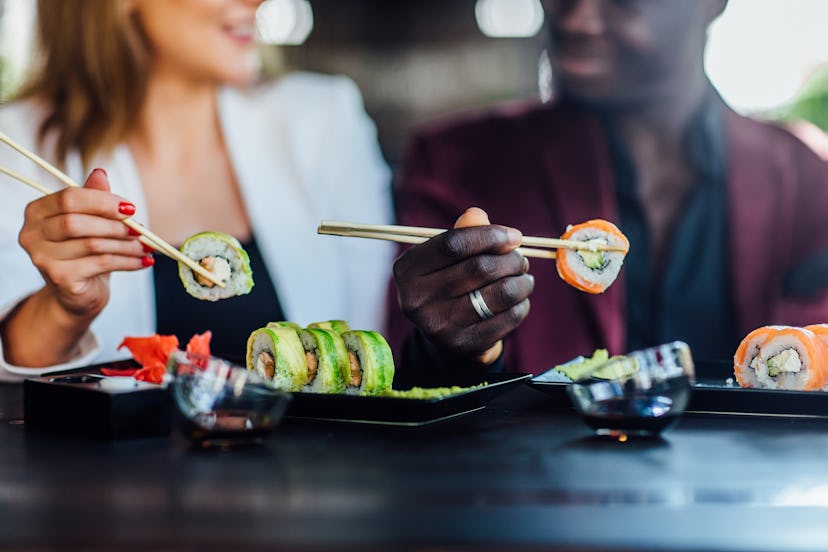 Cropped view of smiling happy couple eating sushi in restaurant, set on table.