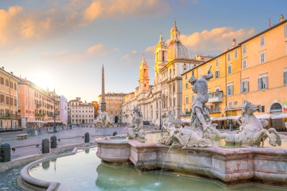 A landscape photo of a fountain, monument, and square in Rome at sunrise. 