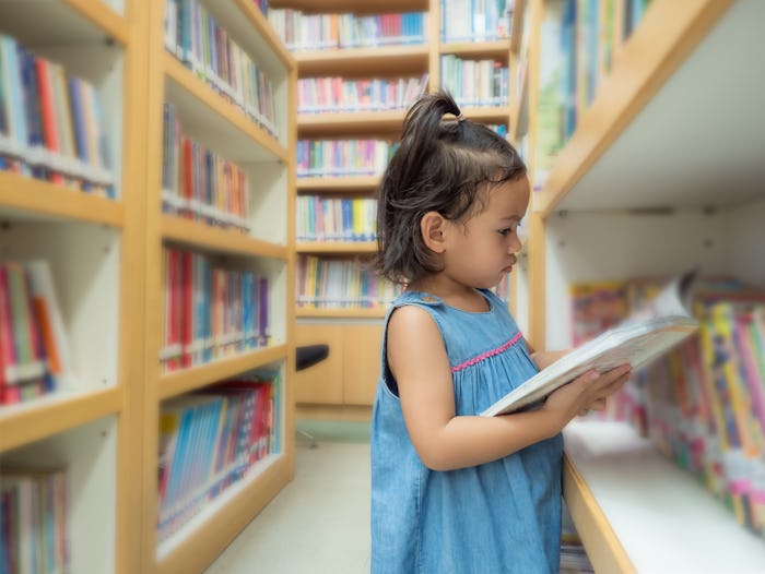Little asian cute girl 3-4 years old looking a kid's book from bookshelf at the library. Learning an...