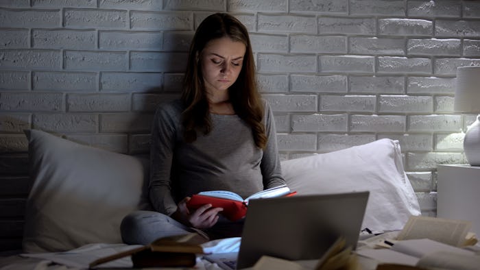 Serious pregnant woman reading books about motherhood, preparing to childbirth