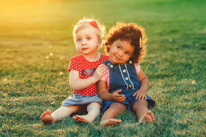 Group portrait of two cute adorable girls toddlers children sitting together. White Caucasian and la...