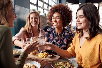 Four young female friends toasting for drinks and food in a restaurant