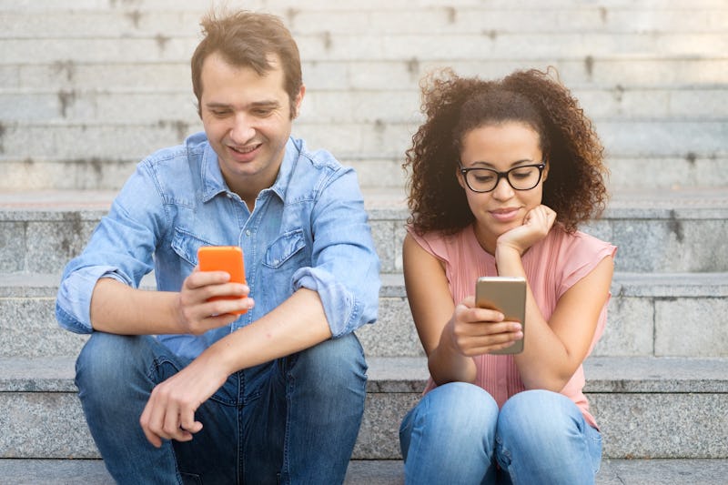 Two friends using their mobile phones seated together