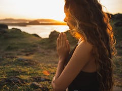 Woman praying alone at sunrise. Nature background. Spiritual and emotional concept. Sensitivity to n...