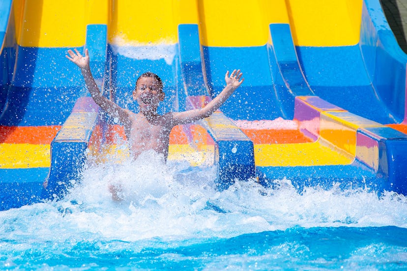 Happy cheerful boy splashing water on water slide at aqua park