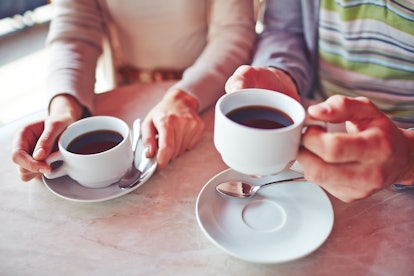 Porcelain cups with hot coffee held by young man and woman
