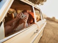 Shot of  young woman taking photos while sitting in a car. Female capturing a perfect road trip mome...