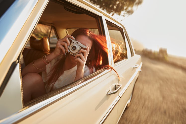 Shot of  young woman taking photos while sitting in a car. Female capturing a perfect road trip mome...