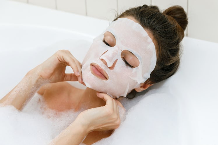 Woman lying in bathtub with a sheet mask on her face