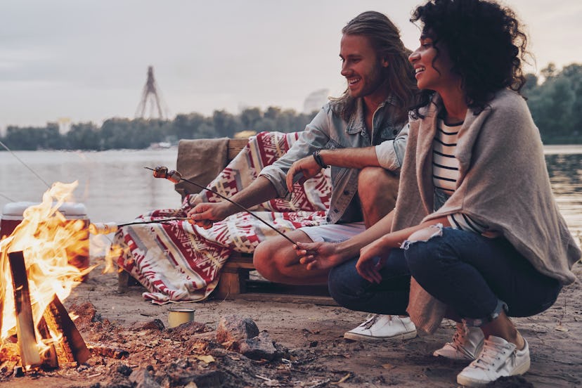 No cares. Group of young people in casual wear roasting marshmallows over a campfire while resting n...