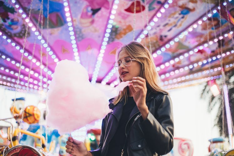 Fashionable young woman in black trendy leather jacket stands in middle of county fair, next to attr...