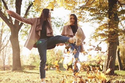 Bottom view of young smiling brunette twin girls having fun and kicking leaves with their feet while...