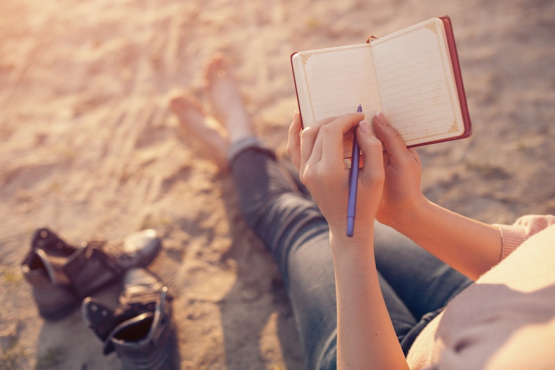 woman writes in diary and sitting on sand; female makes notes and sitting on the beach;