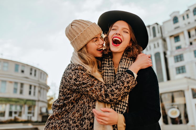 Carefree girl in brown hat embracing her sister. Outdoor photo of happy ladies spending autumn weeke...