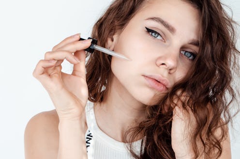 young beautiful curly woman uses white serum for face. The concept of facial skin and hair care.