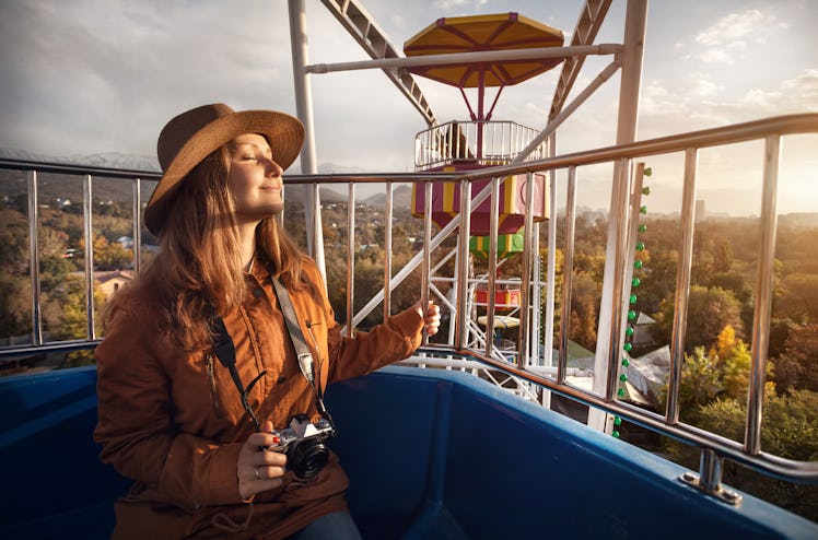 Woman with hat and vintage camera at the cabin of Ferris wheel in the autumn park at sunset