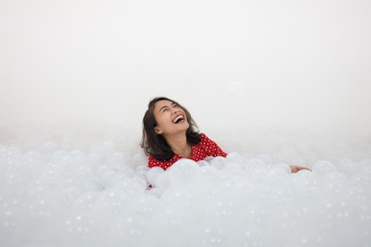 A cute girl with red polka dot t-shirt among the lots of white ball in Ball pit. She feel happy and ...