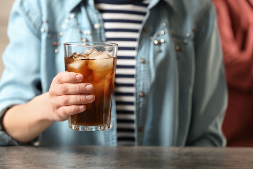 Woman holding glass of cola with ice at table, closeup