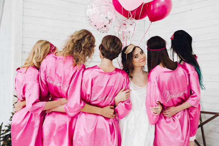 Back view of group of bridesmaids with bride-to-be in beautiful silk robes with different names on t...