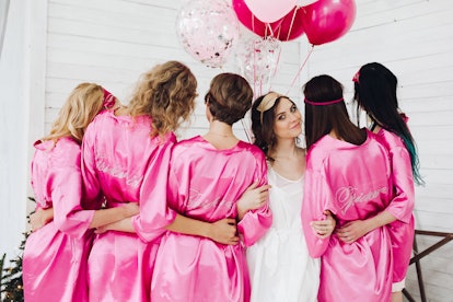 Back view of group of bridesmaids with bride-to-be in beautiful silk robes with different names on t...