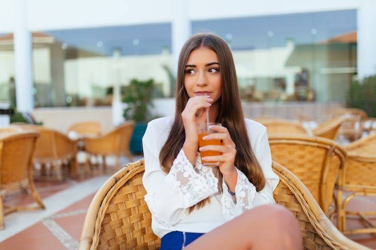 Beautiful young woman sitting in bar cafe, drinking fruit cocktail on a tropical beach