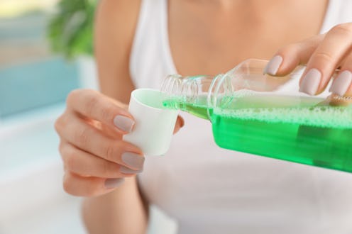 Woman pouring mouthwash from bottle into cap, closeup. Teeth care