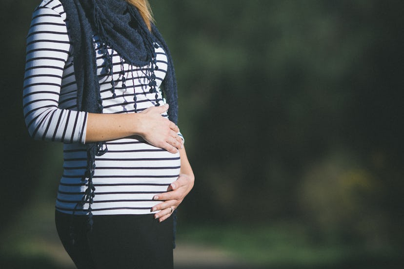 Pregnant woman in stripes with scarf holding belly on a blurred background