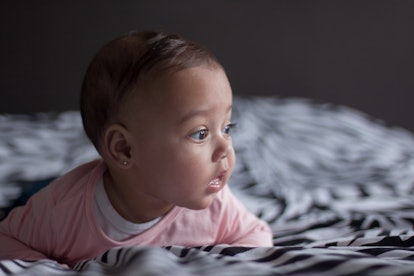 Portrait of a sweet baby girl with beautiful brown eyes with 
a pink shirt lying on parents bed hold...