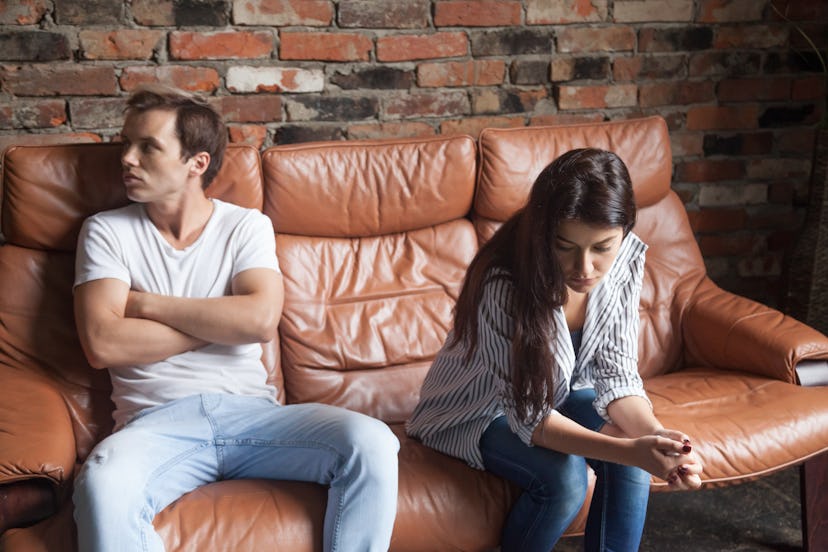 Young man and woman sitting on different sides of each other on couch and not talking. Unhappy coupl...