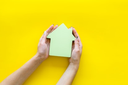 Buy house with house figure in hands on office desk yellow background top view