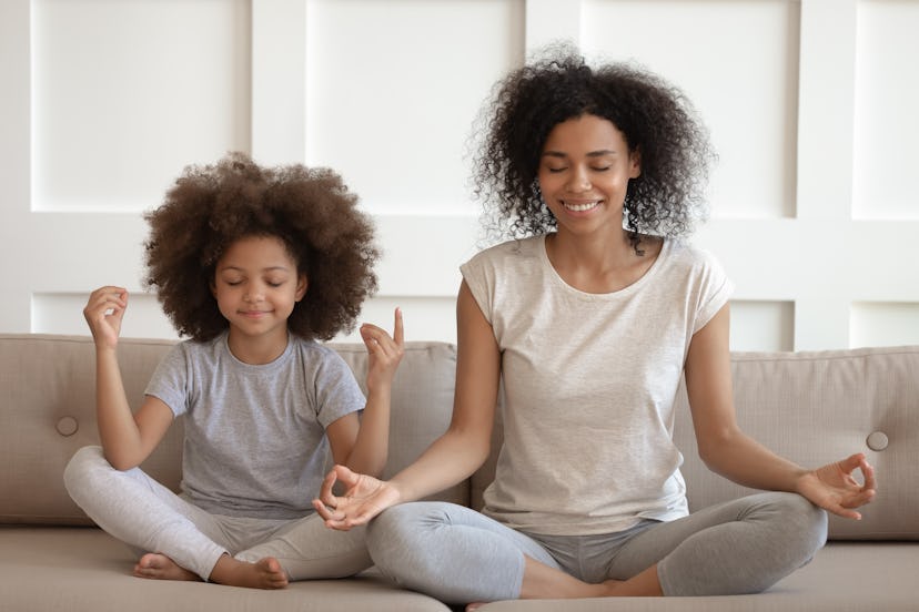 Healthy calm african american mother teaching meditation sit with cute small child daughter on sofa,...