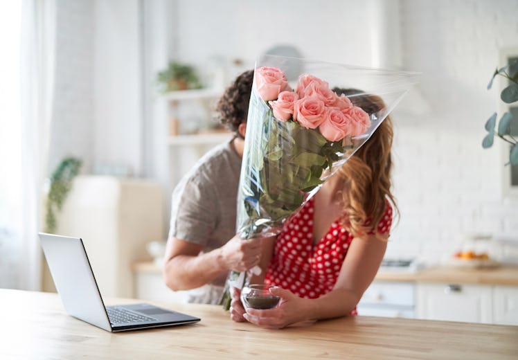 Summer holidays, love, relationship - couple with bouquet of flowers in the kitchen. Laptop on the t...