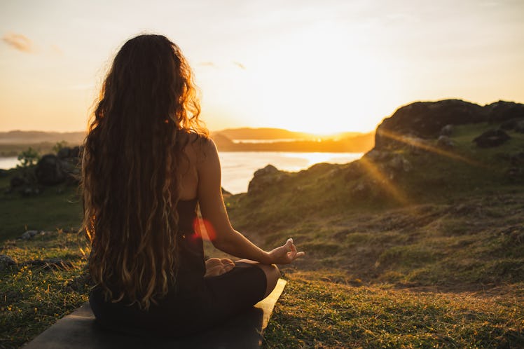 Woman meditating yoga alone at sunrise mountains. View from behind. Travel Lifestyle spiritual relax...