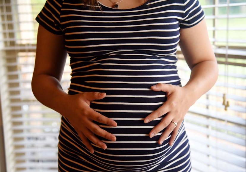 A pregnant woman with hands on belly - in color