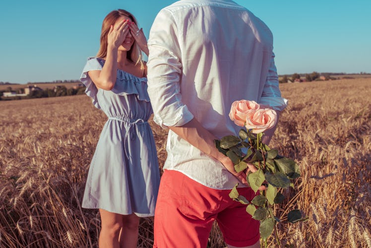 Beautiful and young couple man and woman, summer in a wheat field, behind gift is bouquet of flowers...